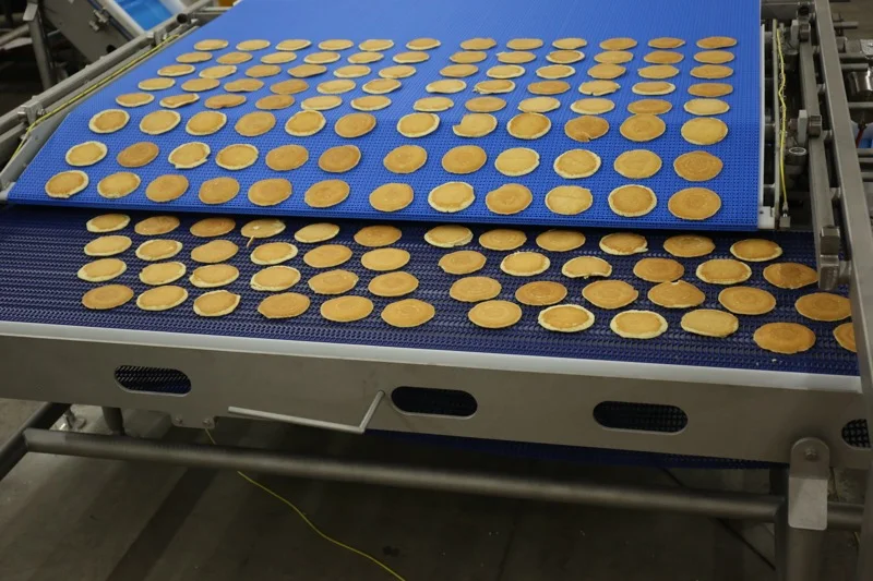 A PFI bakery conveyor transporting individual pancakes onto a secondary conveyor.