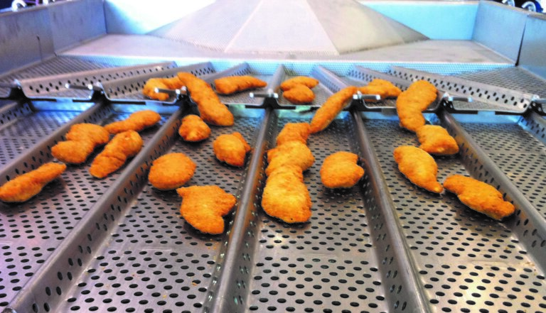A vibratory conveyor evenly distributes frozen chicken nuggets across the processing line.